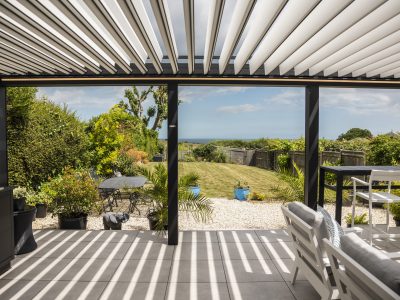 Violux coastal bioclimatic pergola with open white louvres overlooking a seaside garden and ocean view