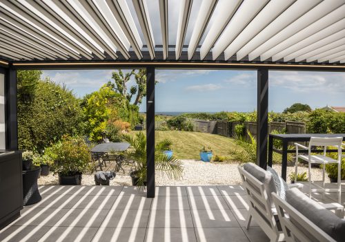 Violux coastal bioclimatic pergola with open white louvres overlooking a seaside garden and ocean view
