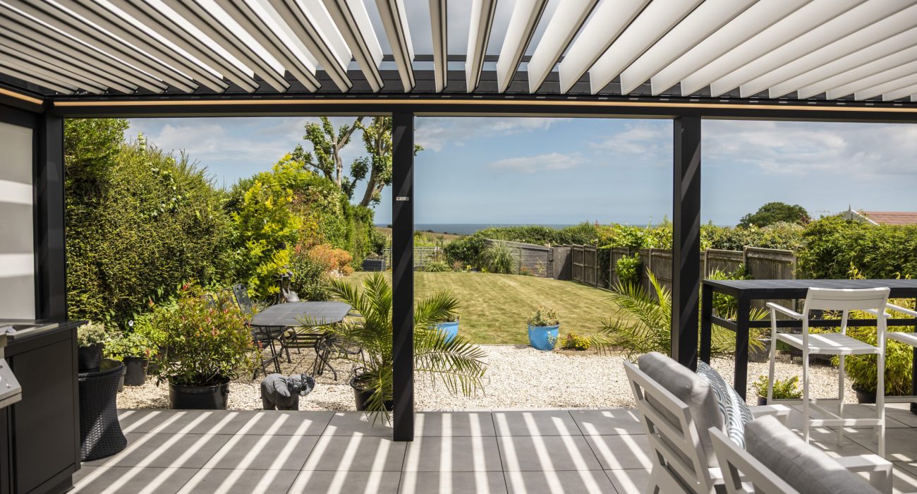 Violux coastal bioclimatic pergola with open white louvres overlooking a seaside garden and ocean view